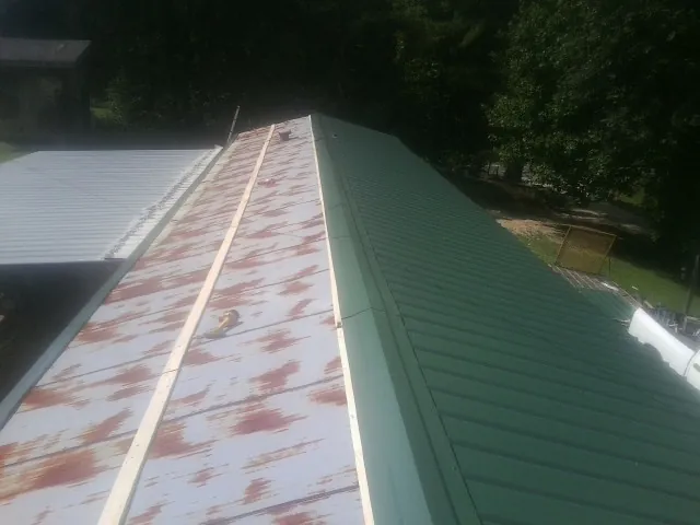 Old rusted panels beside newly installed green metal roofing — Wind Damage Roof Repair by Roofing Brothers in Foster